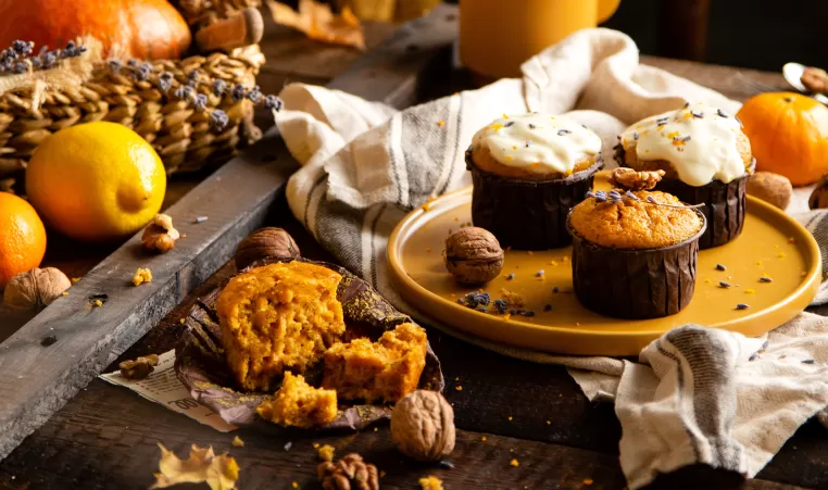 homemade tasty sweet orange pumpkin muffins or cupcakes with white cream, lavender, zest, nuts