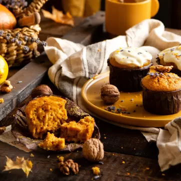 homemade tasty sweet orange pumpkin muffins or cupcakes with white cream, lavender, zest, nuts